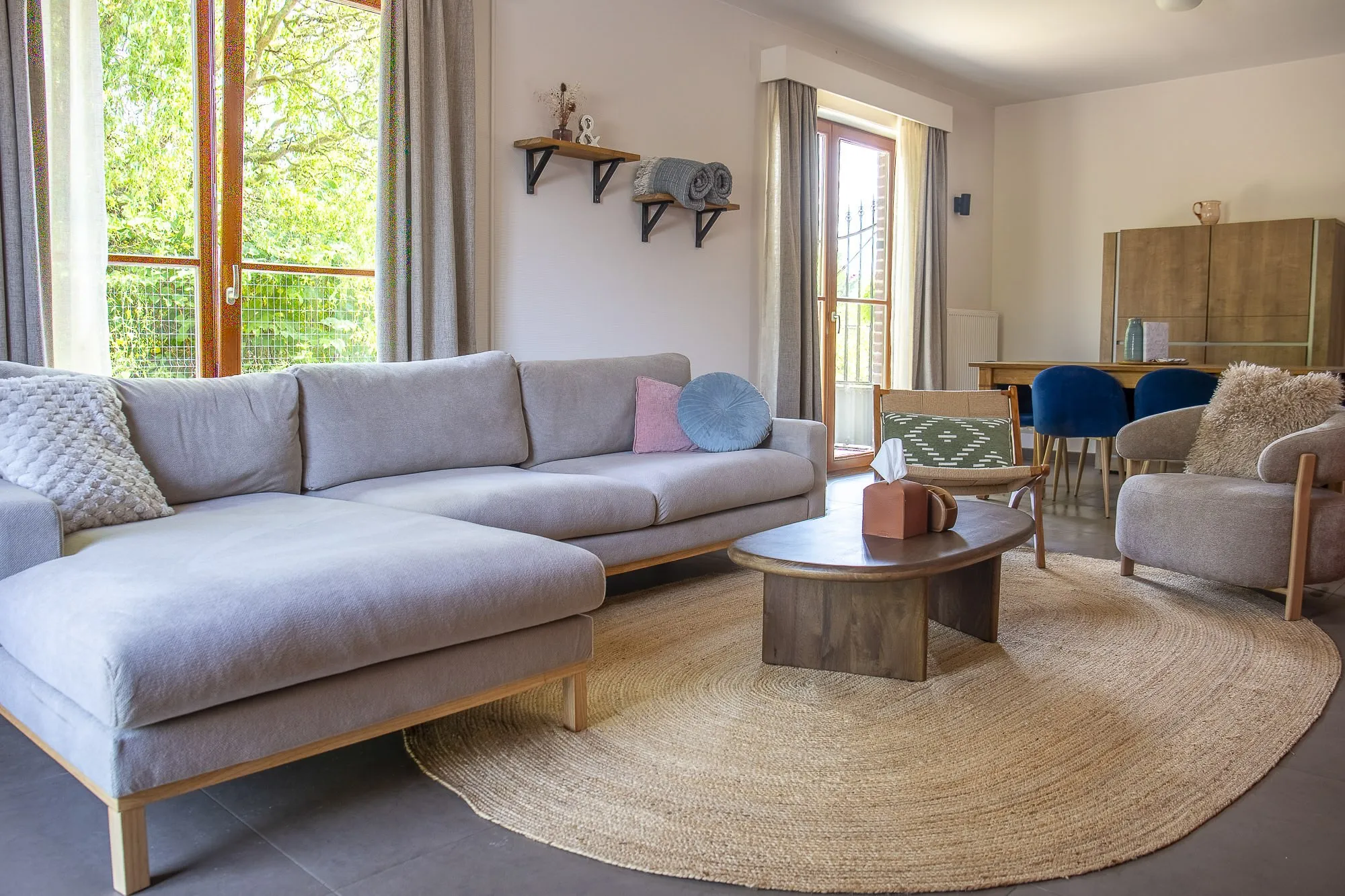 Salon avec canapé gris, espace repas et ouvertures sur le jardin